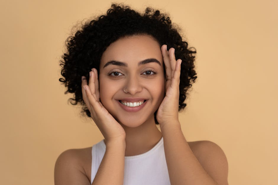 Portrait of a smiling woman with curly hair, highlighting her fresh skin and happiness against a beige backdrop.