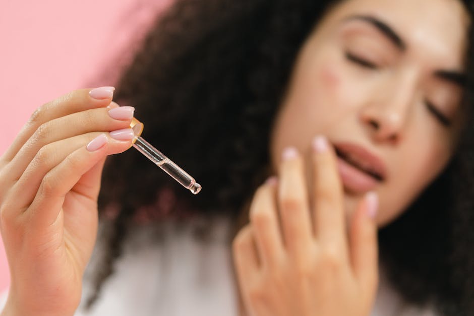 A woman's hand holding a dropper with serum against a blurred face.