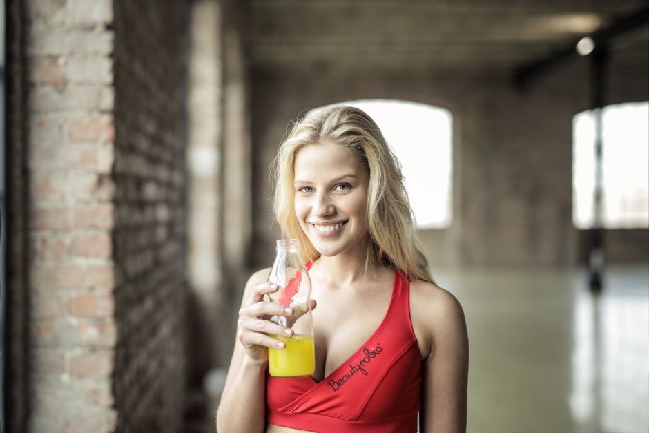 Happy woman in sportswear holding a fresh juice bottle in an urban setting.