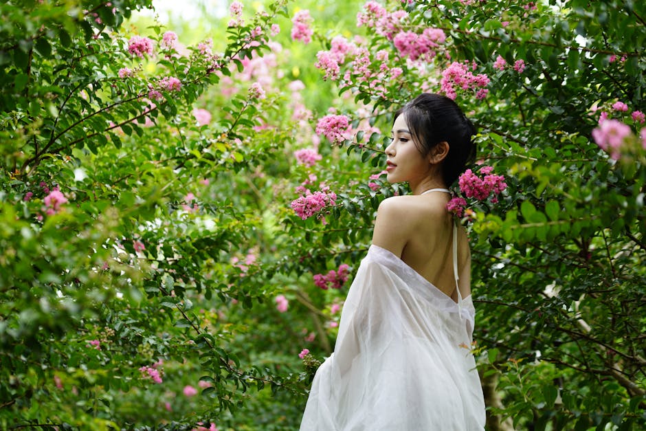 A serene portrait of a woman in a white dress amidst lush blooming pink flowers. Captured outdoors.