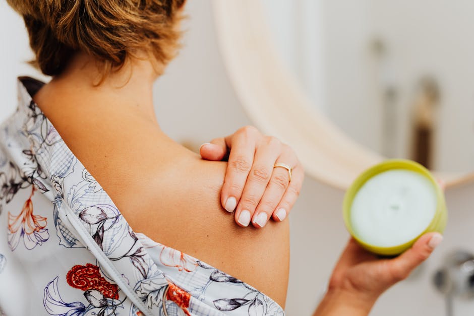Close-up of a woman applying body cream on her shoulder in the bathroom.