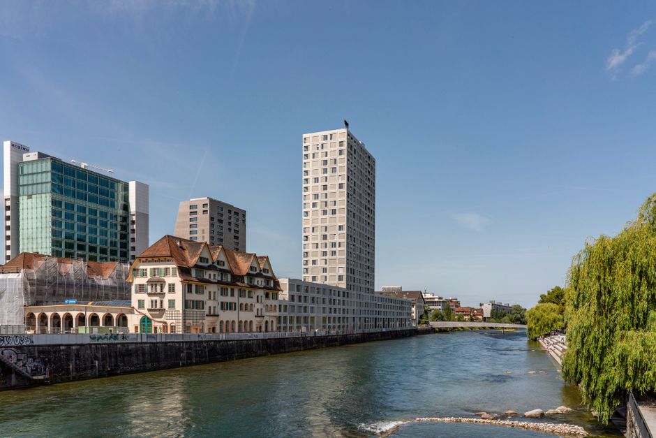 Modern high-rise and traditional buildings by a calm river on a sunny day.