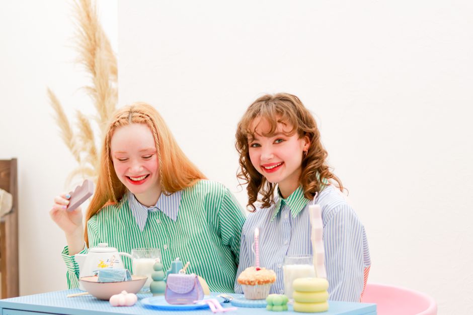 Two smiling girls sitting at a table with cupcakes and drinks, enjoying a cheerful celebration.