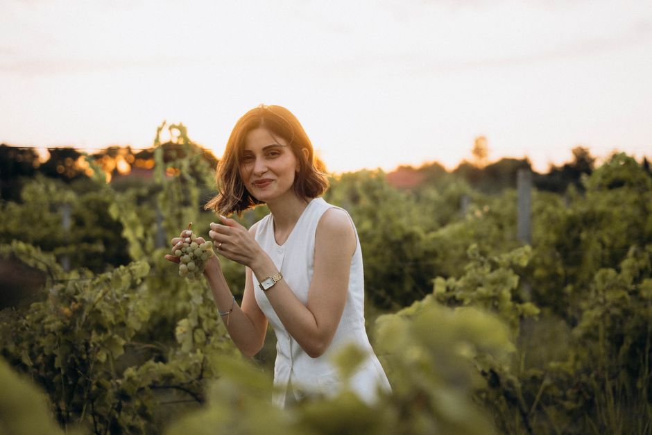 A woman in a vineyard at sunset enjoying fresh grapes and smiling warmly.