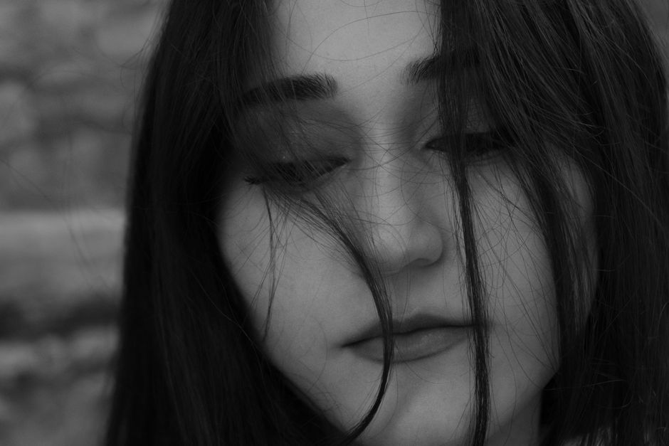Black and white portrait of a woman with hair falling over face, evoking a somber mood.