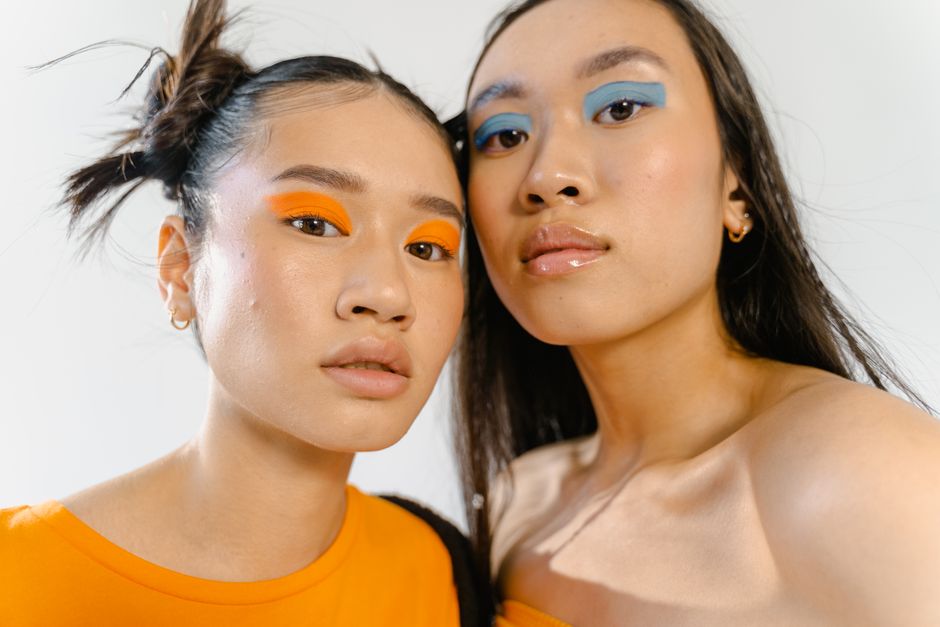 Close-up portrait of two young women with bold eye makeup and fashion-forward style.