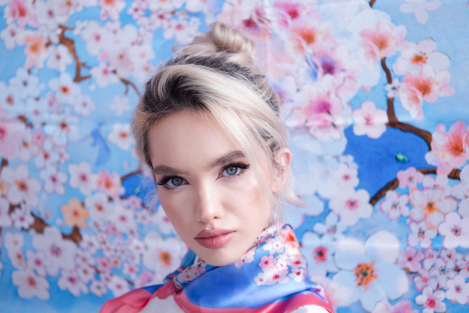 Close-up portrait of a young woman with cherry blossom floral background, embodying modern fashion elegance.
