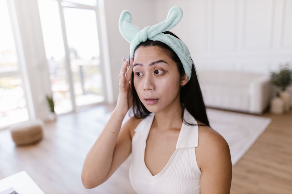Portrait of a young woman in a hairband focusing on her skincare routine in a bright, modern room.