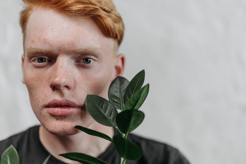 A detailed close-up portrait of a young man with red hair, accented by green leaves, in a studio setting.