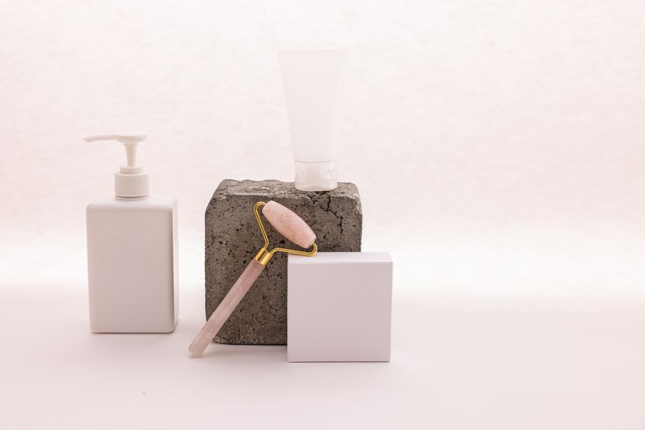 A minimalist beauty set with skincare bottles and a facial roller on a concrete block.