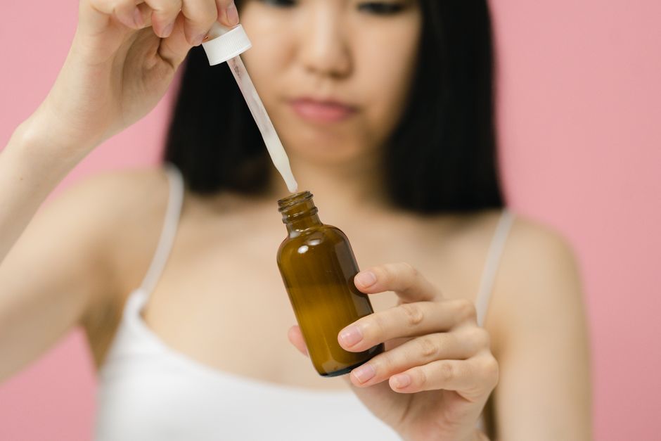 Close-up of a woman applying skincare serum with a pipette against a pink background.