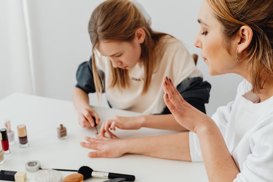 A young girl paints a woman's nails during a home manicure session at a table.