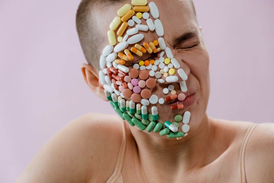 Creative portrait of person with pills covering face, symbolizing medication dependence.