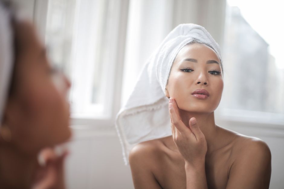 A woman with a towel on her head admires her reflection in a bright, elegant setting.