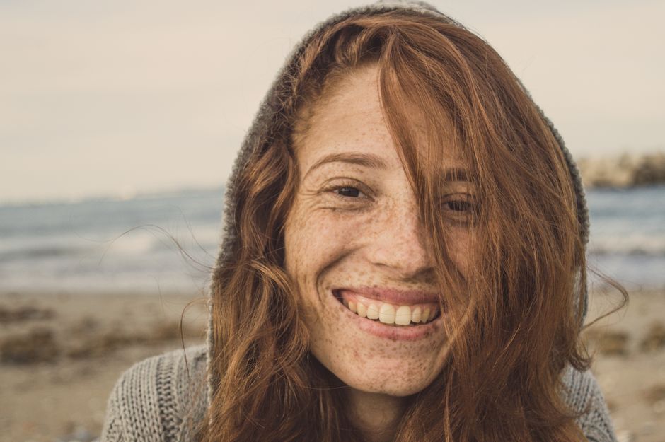 Close-up portrait of a smiling redhead woman at the beach on a sunny day.
