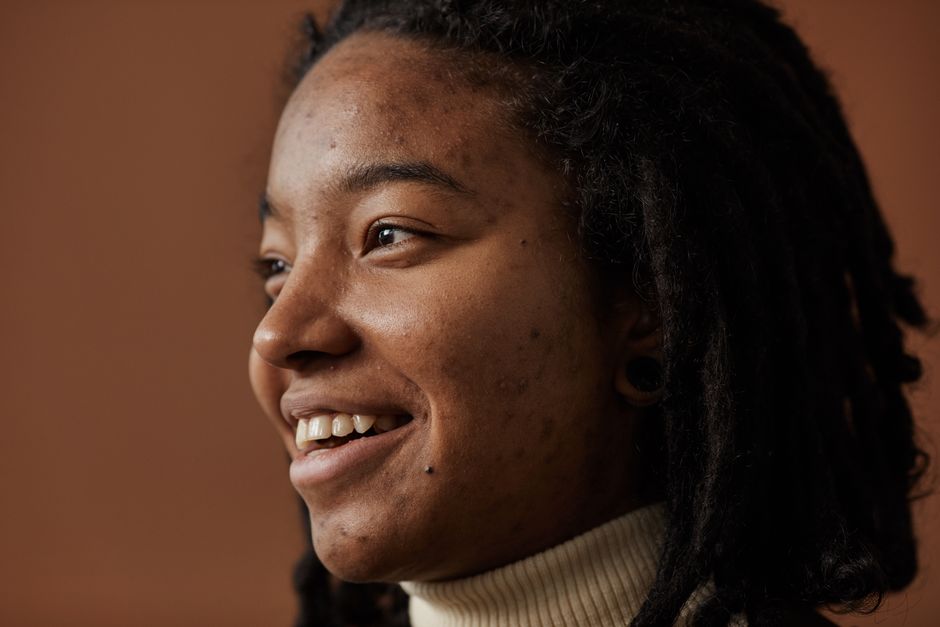 A side profile of a person smiling, showcasing natural dreadlocks and a warm, authentic expression.