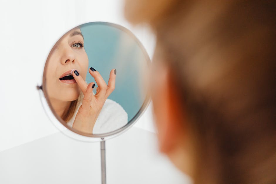 Woman applying skincare cream to her lips in front of a mirror, indoors.