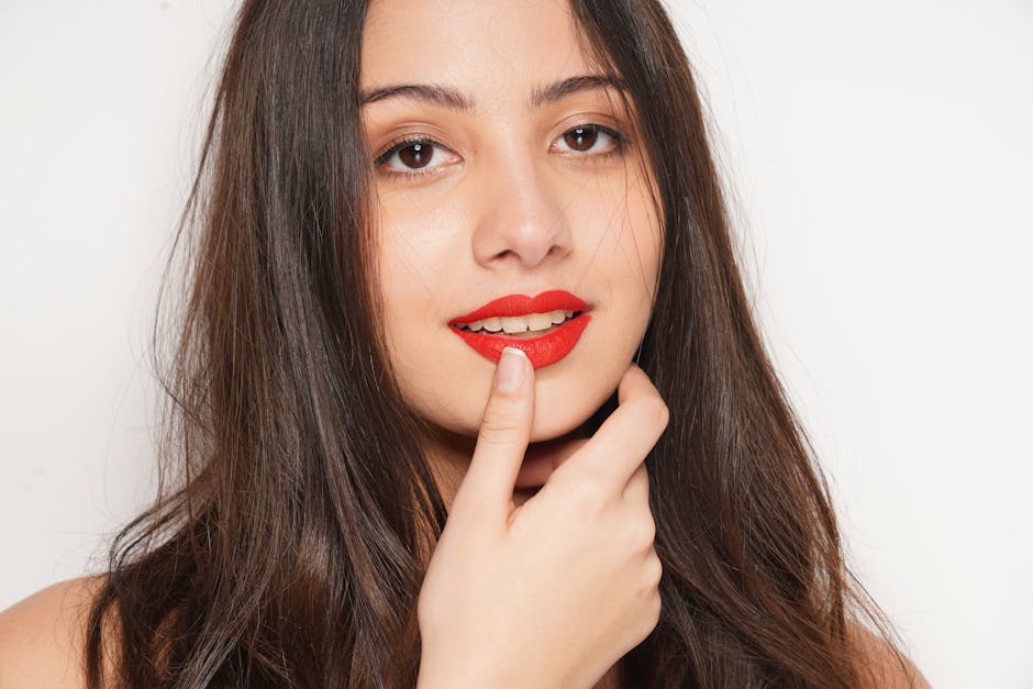 Close-up of a smiling young woman with red lipstick on a white background, showcasing elegance and beauty.