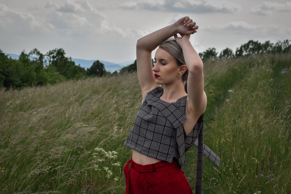 Woman with arms raised in grassy field, showcasing fashion and carefree vibes.