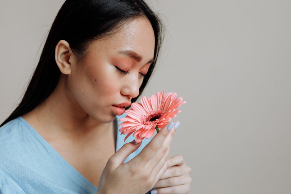 Closeup of an Asian woman gently smelling a pink Gerbera daisy, eyes closed in peaceful contemplation.