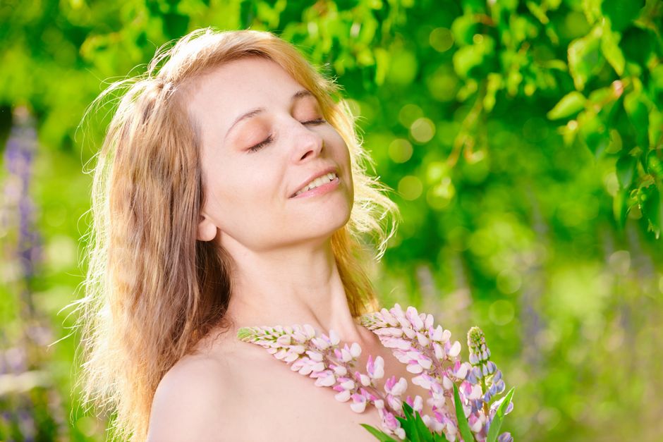 A peaceful woman enjoying a sunny day in a vibrant green garden, holding flowers.