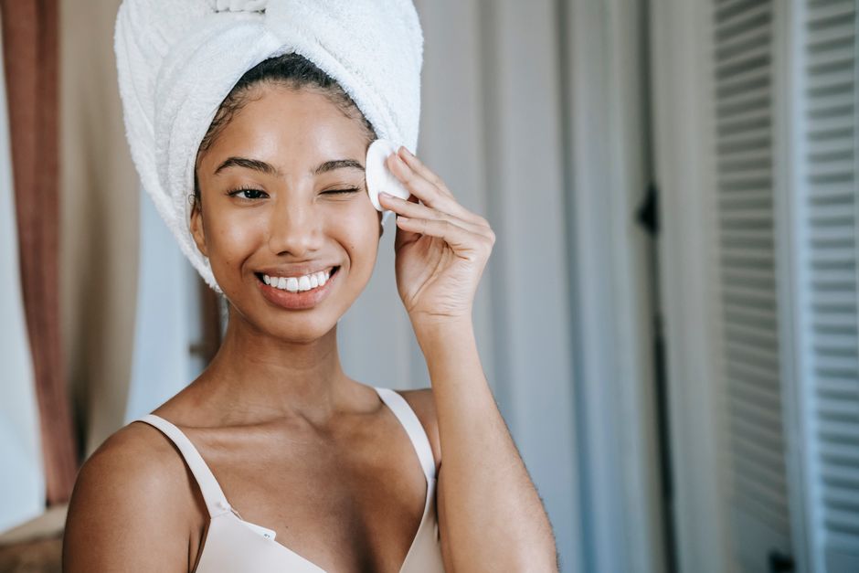 Cheerful ethnic woman cleaning face with cotton pad while doing daily beauty routine in bathroom