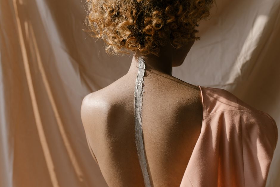 Creative studio portrait of a woman with curly hair, back view, featuring conceptual body art.