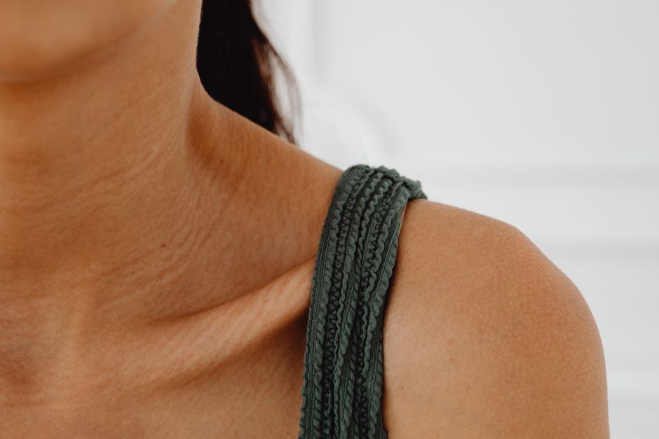 A detailed close-up of a woman's shoulder wearing a textured green tank top.