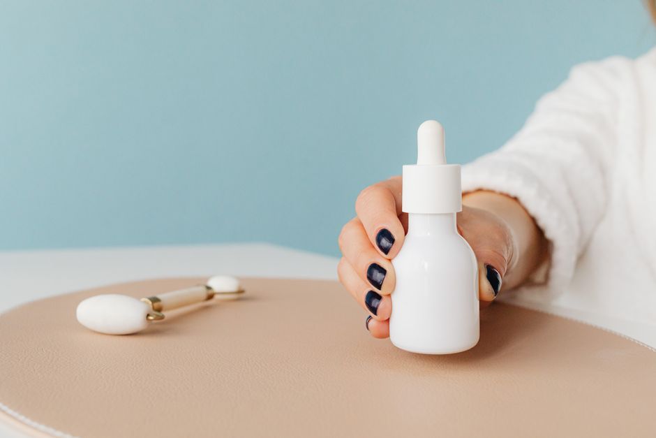 Close-up of a hand holding a serum bottle with a jade roller, ideal for skincare routines.