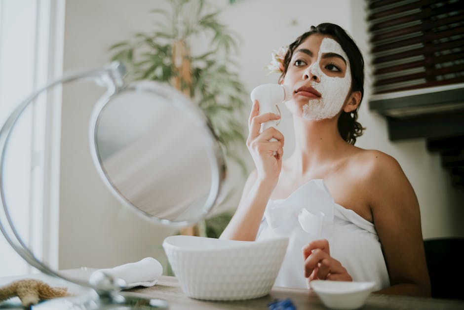 Young woman applying face mask with a facial brush indoors, enhancing skincare routine.