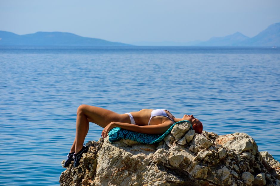 Woman sunbathing on a rock by the sea in Tučepi, Croatia, enjoying a sunny summer day.