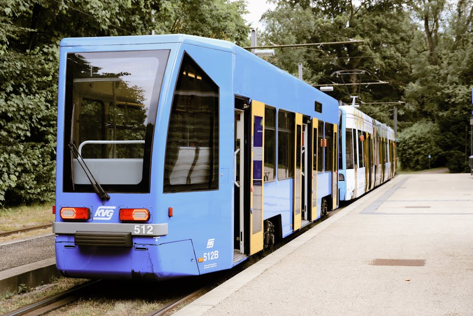 A blue tram is stopped at a station in Kassel, Hessen, Germany, surrounded by lush greenery.