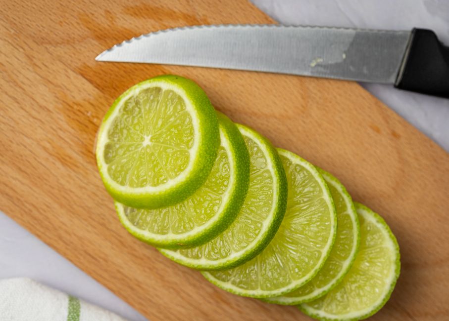 Close-up of sliced lime on a wooden board with a knife, perfect for culinary use.